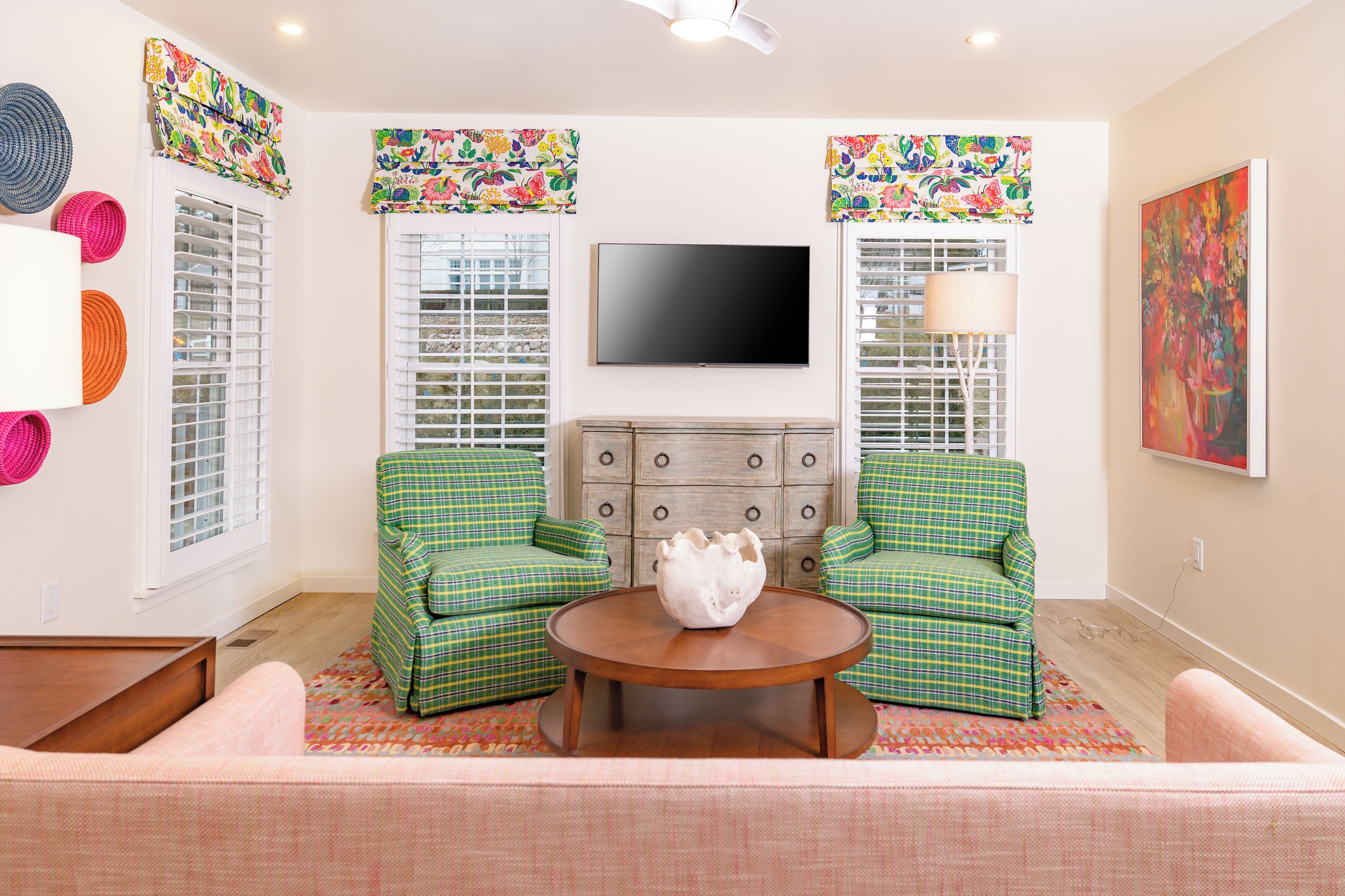 A living room with two green plaid armchairs, a wooden coffee table, a flat-screen TV, and a decorative wall piece.