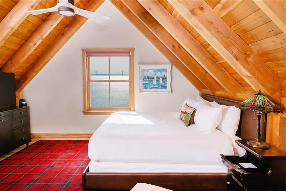 Une chambre à coucher comprenant un lit, une table de chevet, une lampe, une commode, une fenêtre avec vue et un ventilateur de plafond.