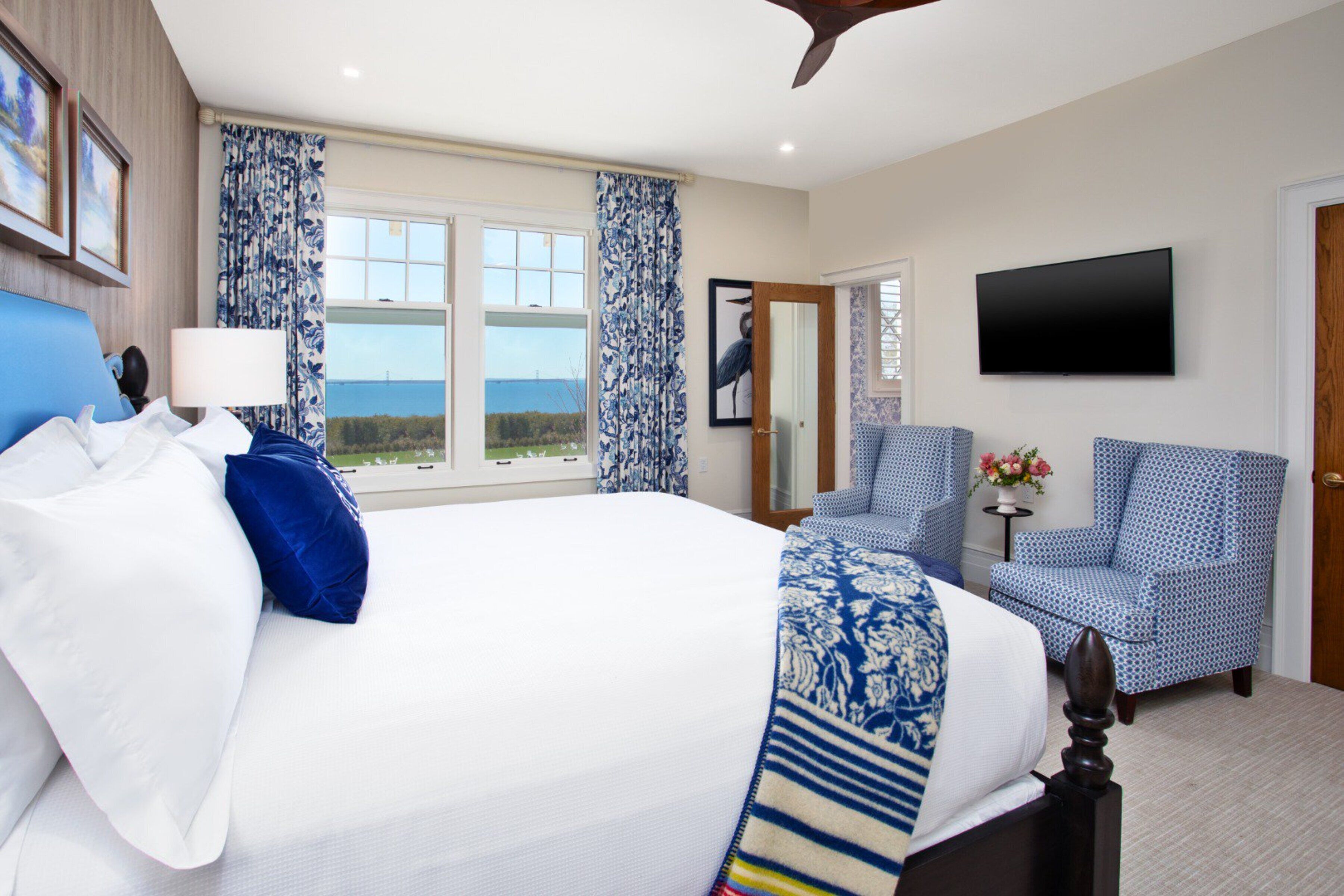 Quarto de hotel com uma cama grande, televisão, cadeira e vista para o mar.