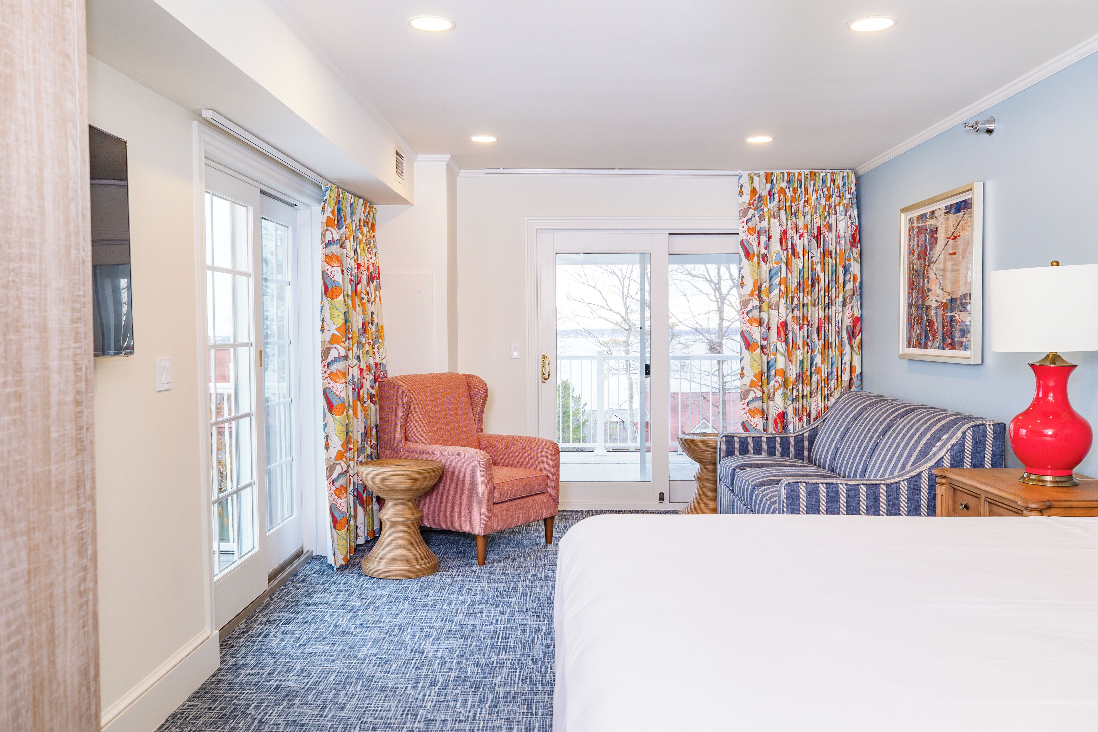 A hotel room with a bed, a chair, a sofa, a lamp, and a window with curtains.