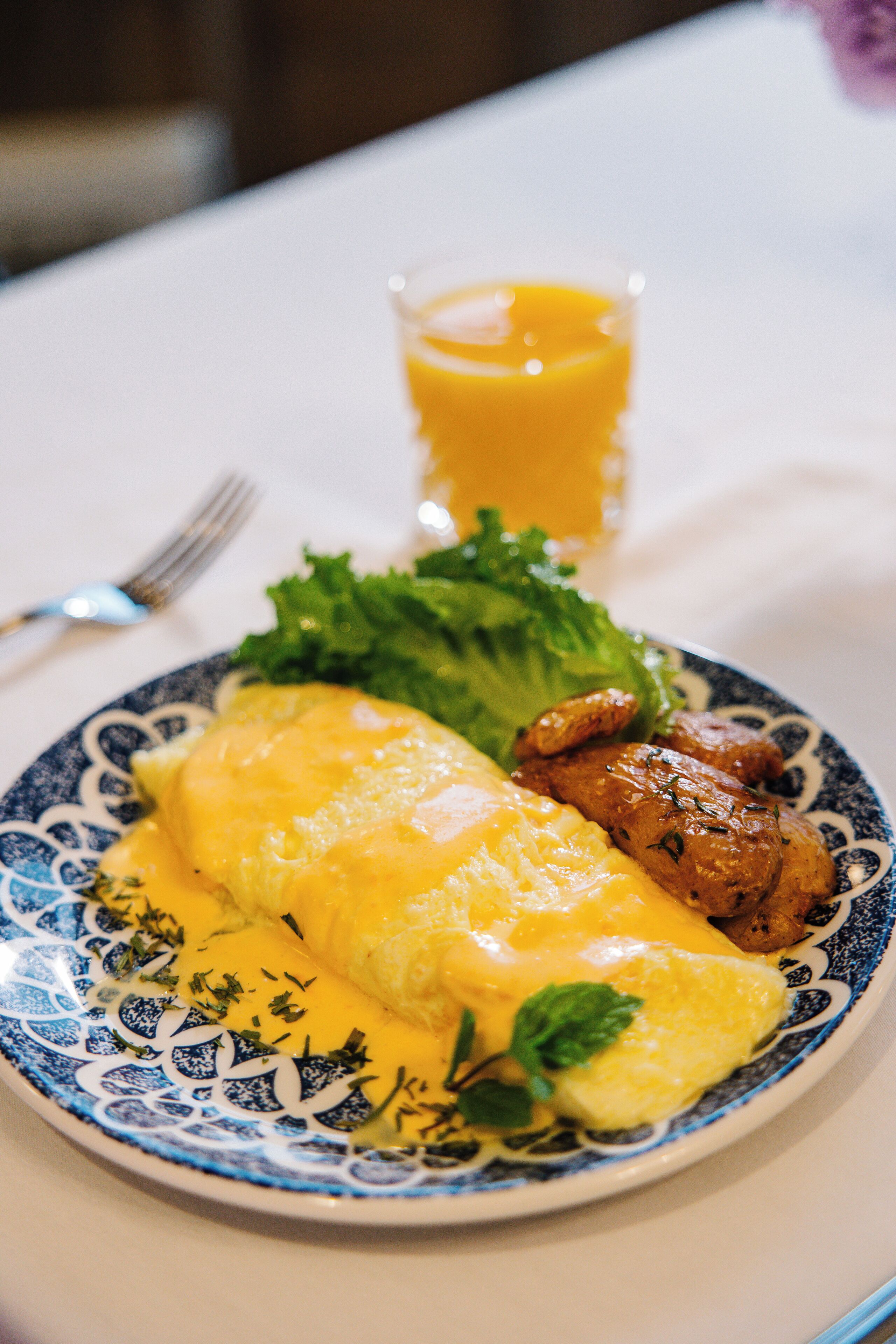 A plate with an omelette, meat, and lettuce, accompanied by a glass of orange juice.