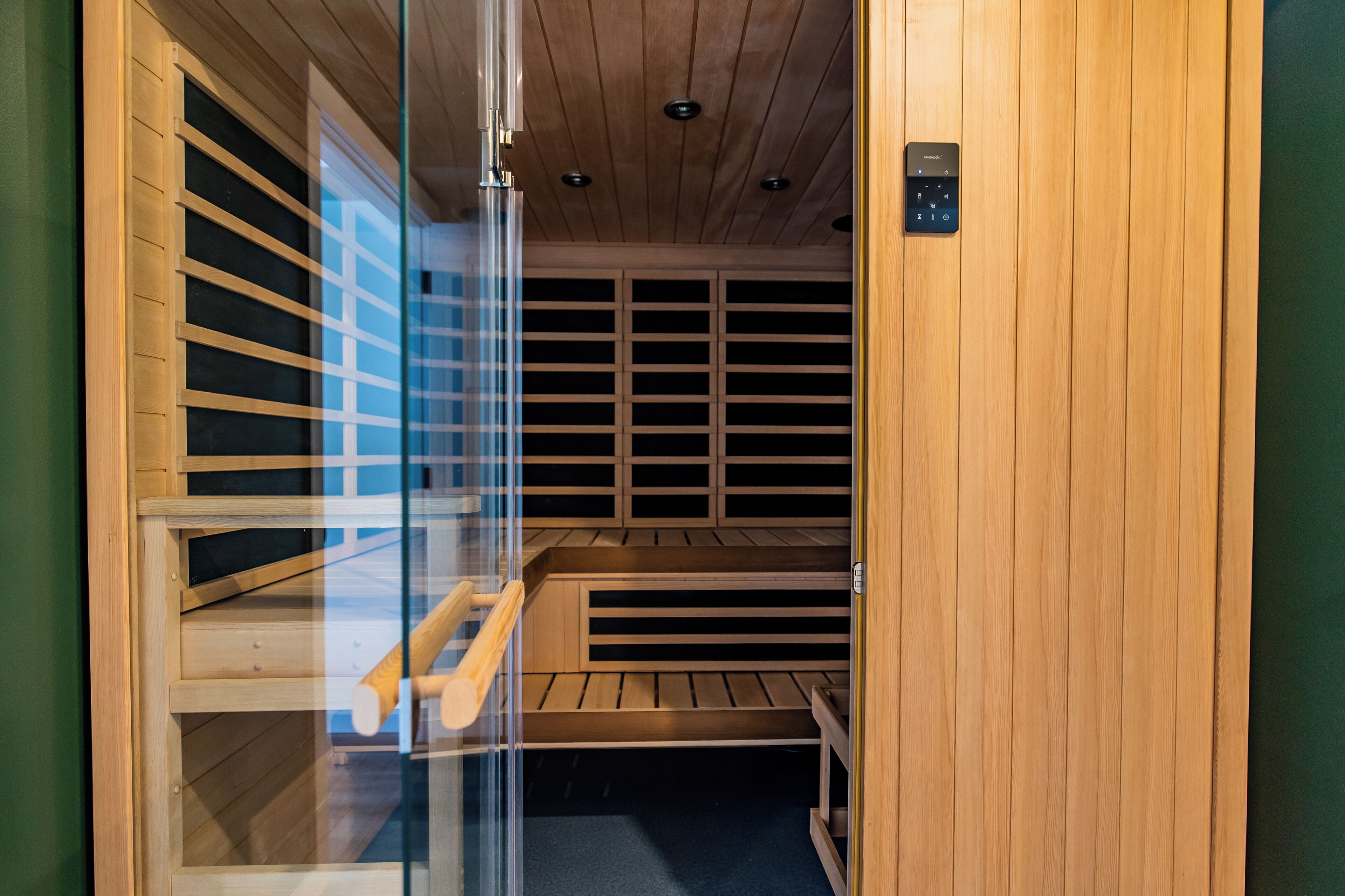 A sauna with wooden benches and a glass door, featuring a control panel on the wall.