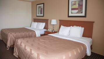 Habitación de hotel con dos camas, una mesita de noche con lámpara y cuadros en las paredes.