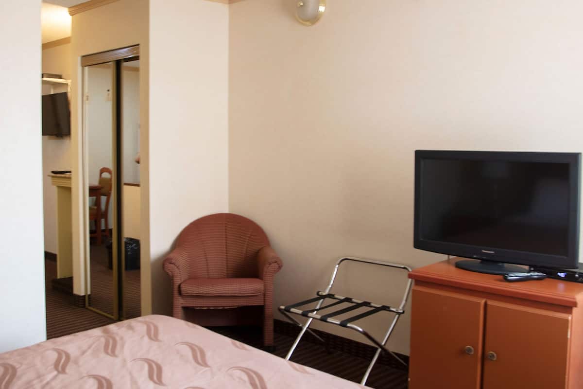 Quarto de hotel com cama, televisão, cadeira e guarda-roupa.