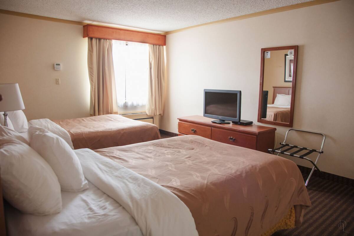 Quarto de hotel com duas camas, televisão, penteadeira e janela com cortinas.