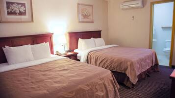 A hotel room with two beds, a nightstand, a lamp, and a framed picture on the wall.