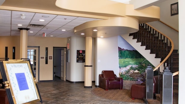 A spacious lobby with a curved staircase, a seating area, and a decorative wall mural. - All Stay Suites (Westlock)