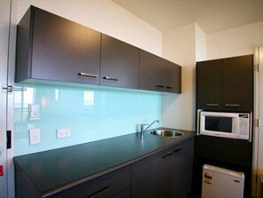 A compact kitchen with dark cabinets, a stainless steel sink, and a microwave.