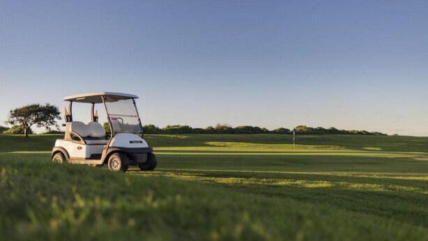 Un carrito de golf sobre un campo verde, con una bandera al fondo.