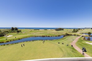 A golf course with a pond, a walking path, and a view of the sea.