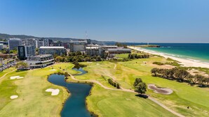 Golfkenttä, jossa on vesialue, ja joka sijaitsee aivan rannan ja kaupunkirakennusten vieressä.