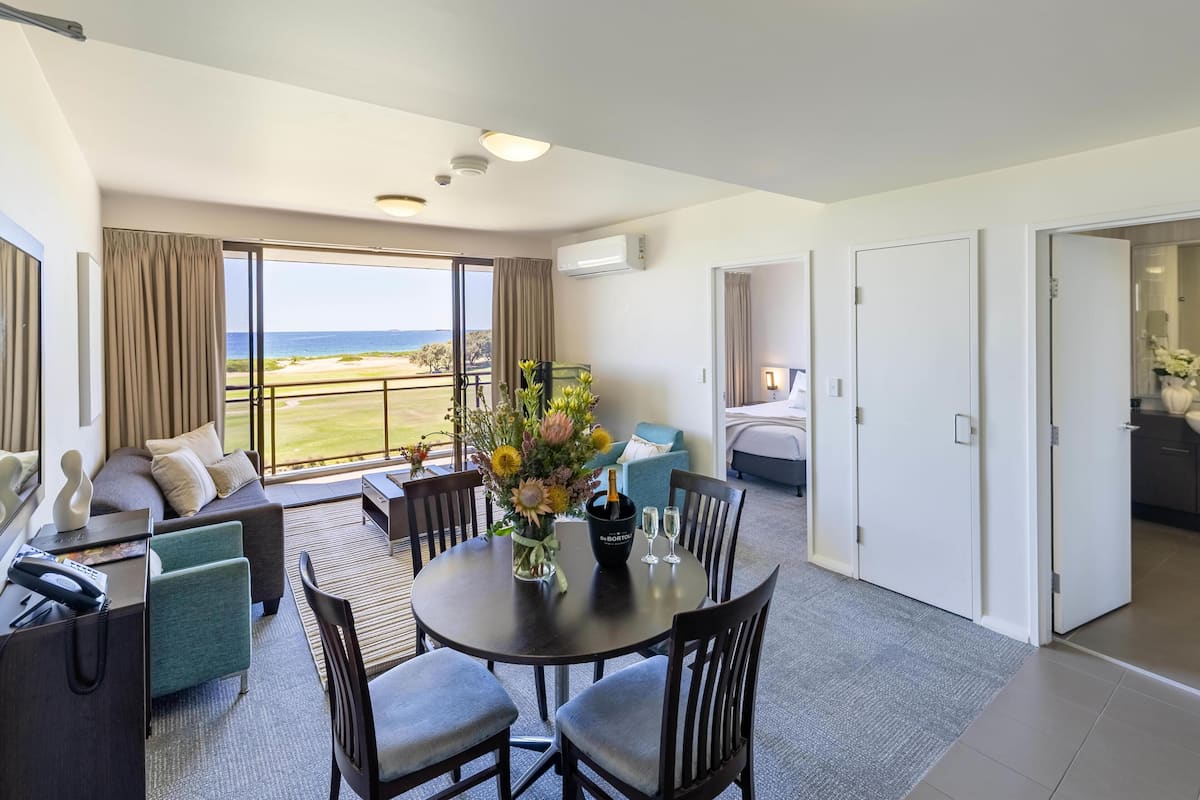 A hotel room with a balcony, a dining area, and a bed.