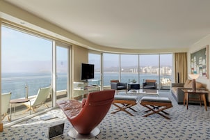 Amplio salón con un gran ventanal que ofrece vistas a la ciudad, un televisor de pantalla plana y asientos cómodos.