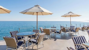 Una terraza con sillas y mesas de mimbre, grandes sombrillas y vista al mar.
