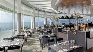 Un restaurante moderno con vistas al mar, que cuenta con techos altos, ventanas amplias y una zona de bar central.