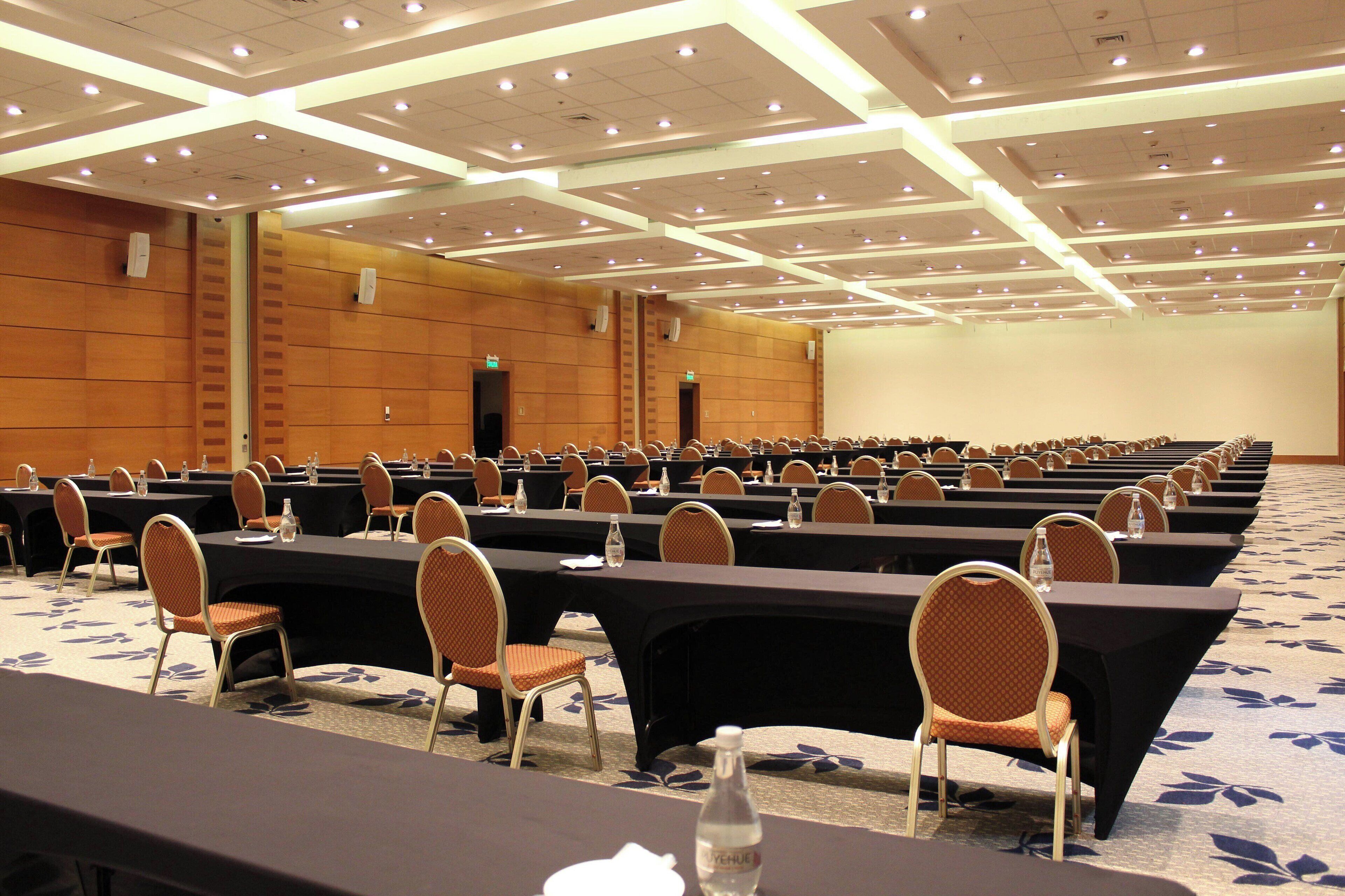 Un salón de conferencias con filas de mesas y sillas, equipado con botellas de agua y tarjetas de identificación.