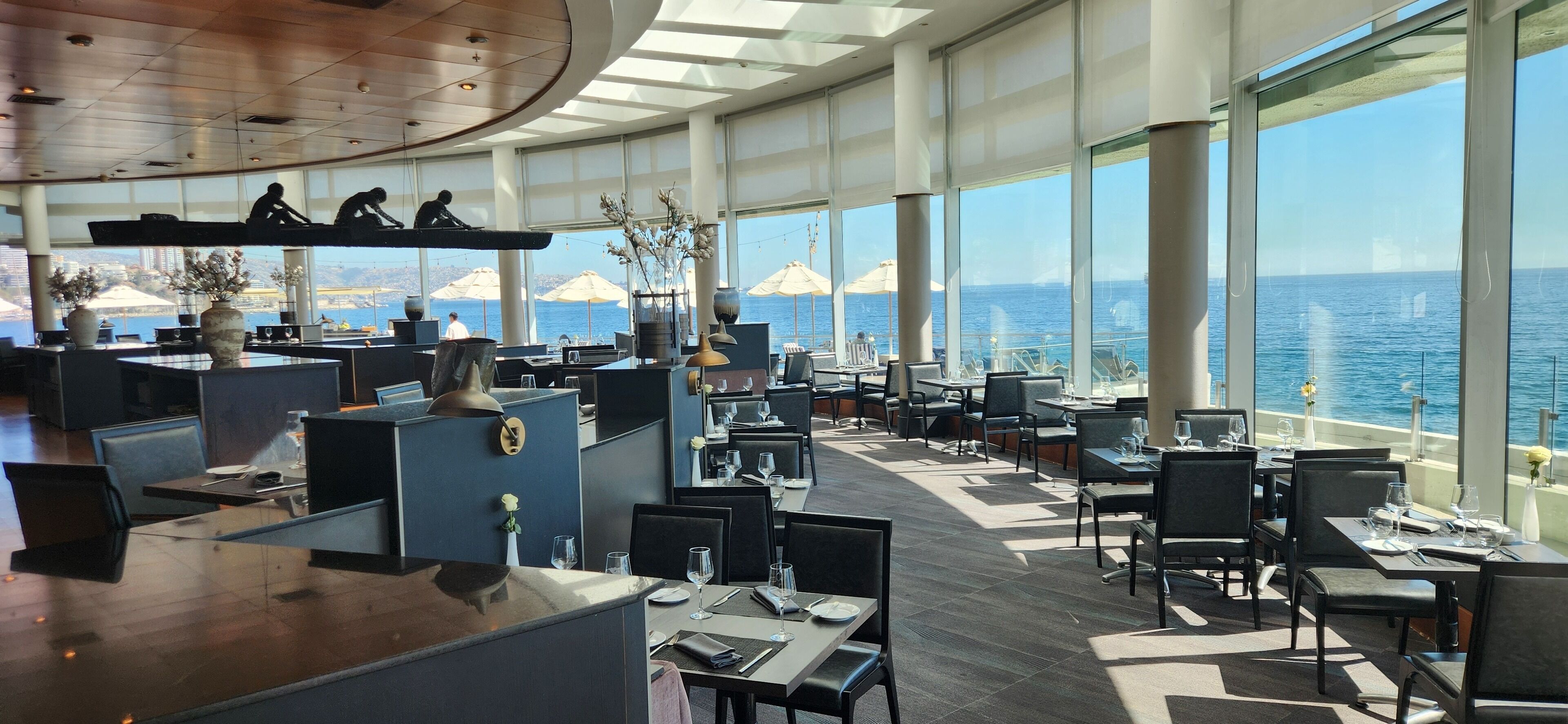 A modern restaurant with high ceilings, large windows, and a view of the ocean.