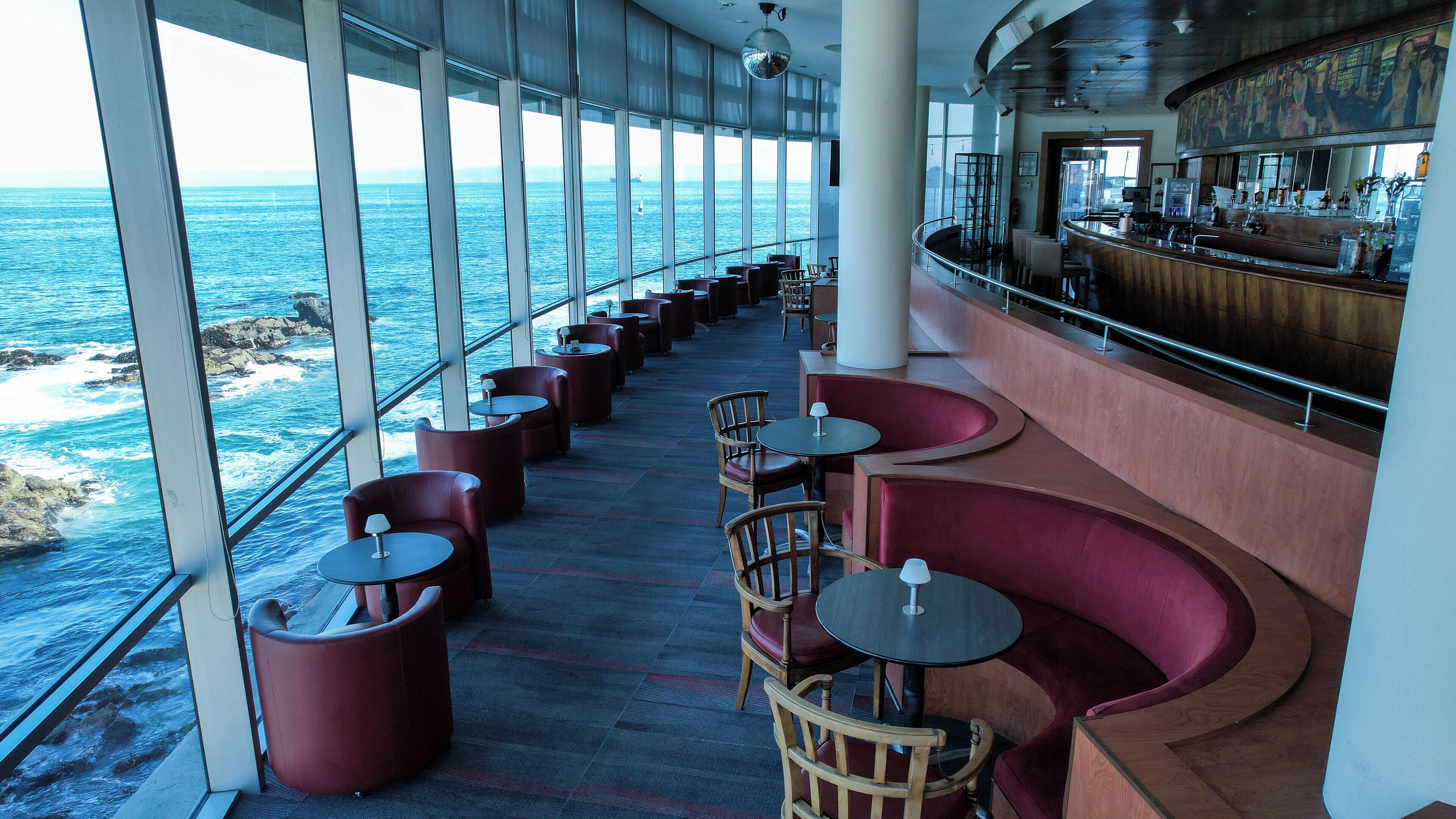 A bar area with seating along a railing overlooking the ocean.