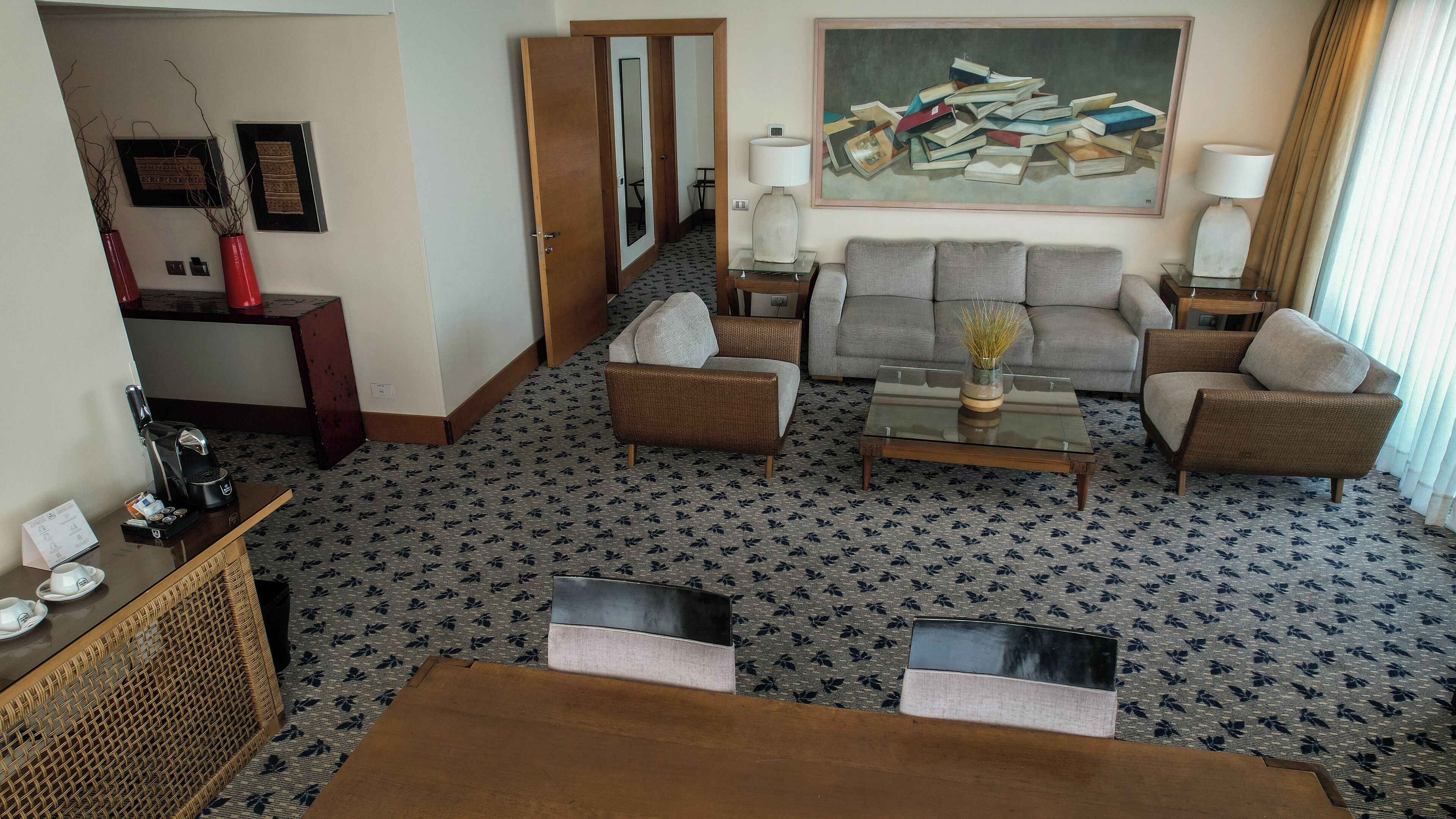 Une chambre d’hôtel dotée d’un coin salon comprenant un canapé, une table basse et un tableau représentant des livres, accroché au mur.