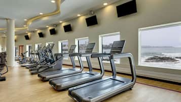 Un gimnasio con cintas de correr a lo largo de una pared con grandes ventanales que dan a una masa de agua.