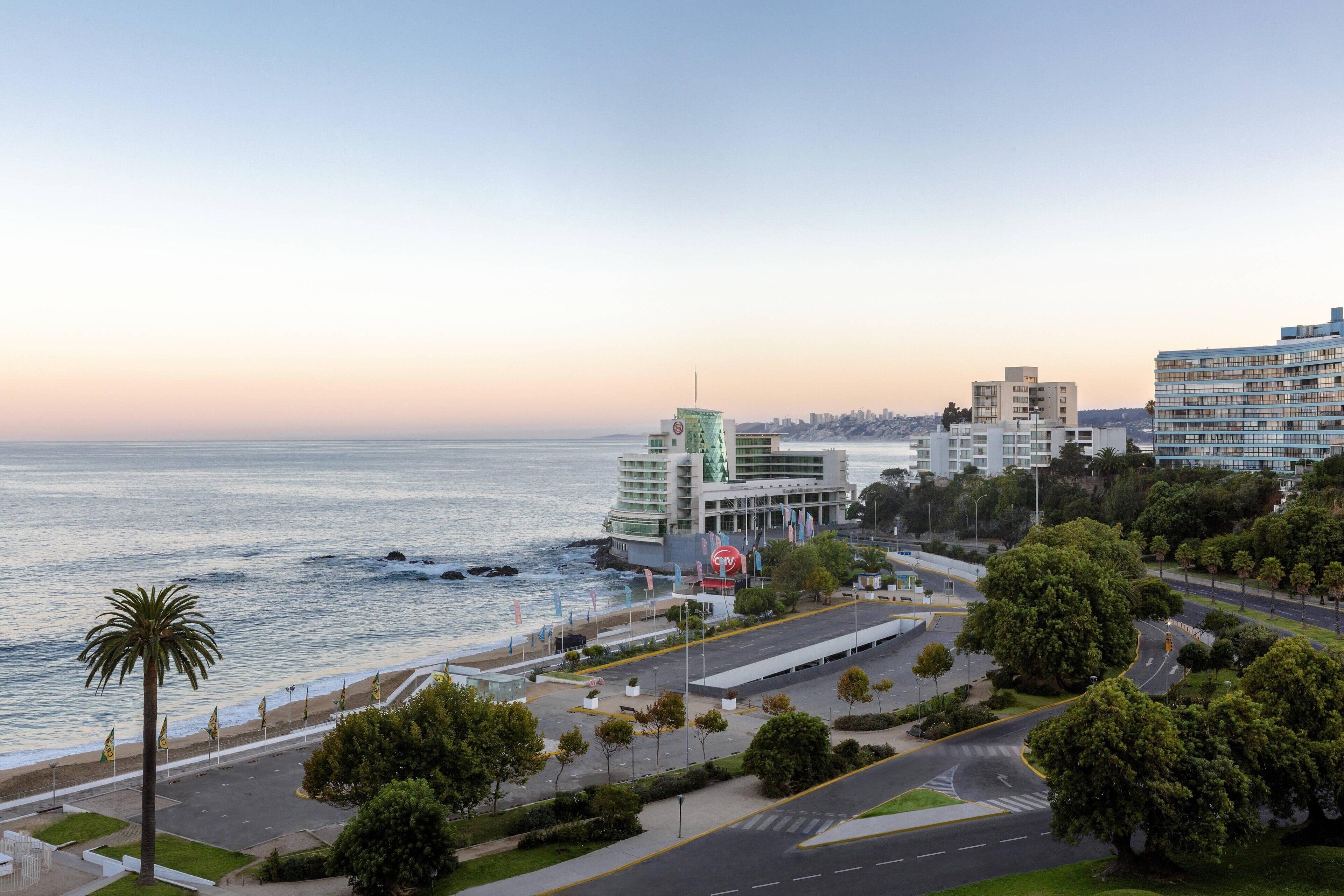 Un paisaje urbano costero con edificios modernos, un puerto deportivo y una carretera que lleva a una zona de playa.