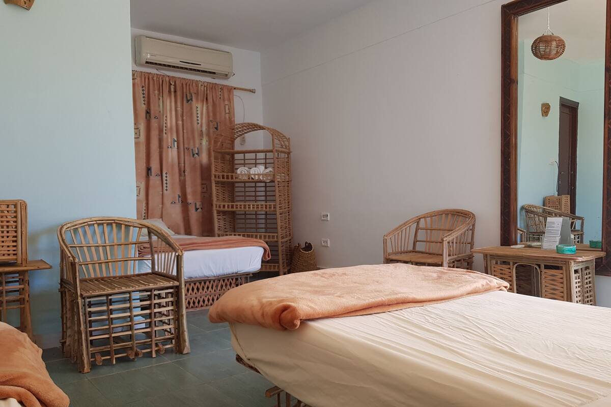 Een kamer met een bed, twee rieten stoelen, een kleine tafel en een spiegel.