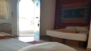 Una habitación con dos camas, una silla de madera, un tapete rojo y un tapiz decorativo en la pared.