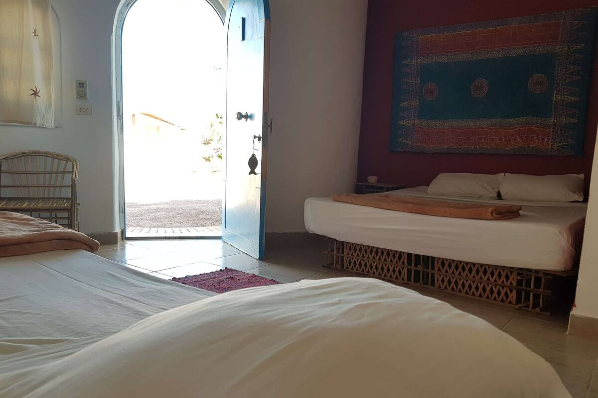 Een kamer met twee bedden, een houten stoel, een rode mat en een behang met patroon aan de muur.