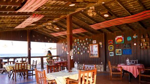 Un restaurante con mesas y sillas de madera, vista al océano y varios platos decorativos en las paredes.