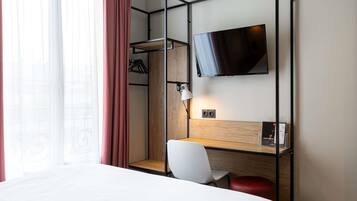 Een hotelkamer met een bed, een bureau met stoel, een aan de muur bevestigde televisie en een raam met gordijnen.