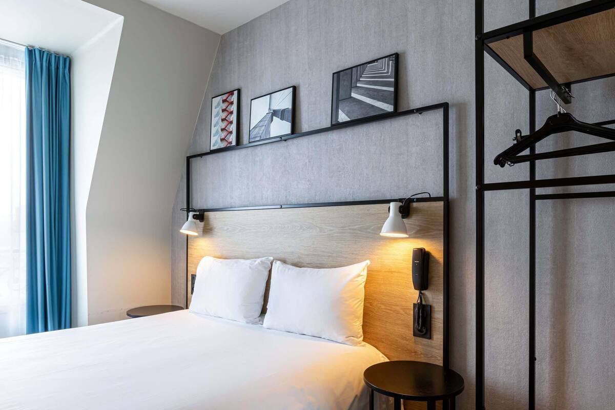 Ein modernes Hotelzimmer mit einem großen Bett, Nachttischen, einem fest montierten Telefon und Kunstwerken an der Wand.