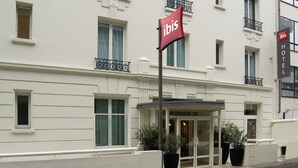 A white hotel with a red ibis sign, large windows, and potted plants at the entrance. - ibis Paris Boulogne Billancourt (Boulogne-Billancourt)