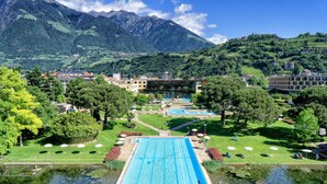 A hotel with a swimming pool, surrounded by lush greenery and mountains. - Hotel Therme Meran - Terme Merano (Merano)