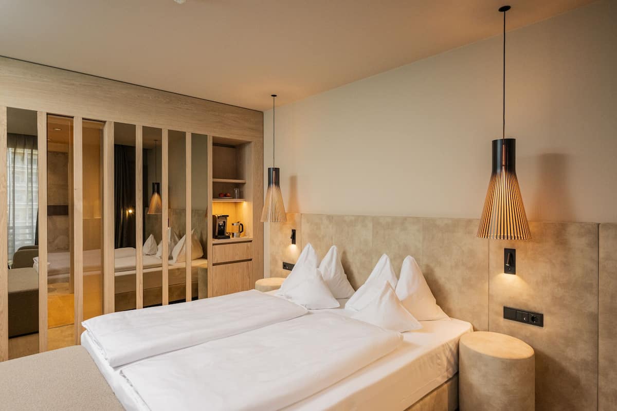 A modern hotel room with a large bed, wooden panel dividers, a built-in desk, and pendant lighting.