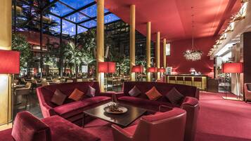 A spacious lobby with red sofas, a central table, and a glass ceiling allowing natural light.