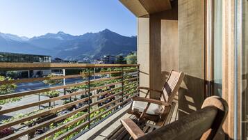 A balcony with a wooden chair, a view of mountains, and a building with a glass facade.