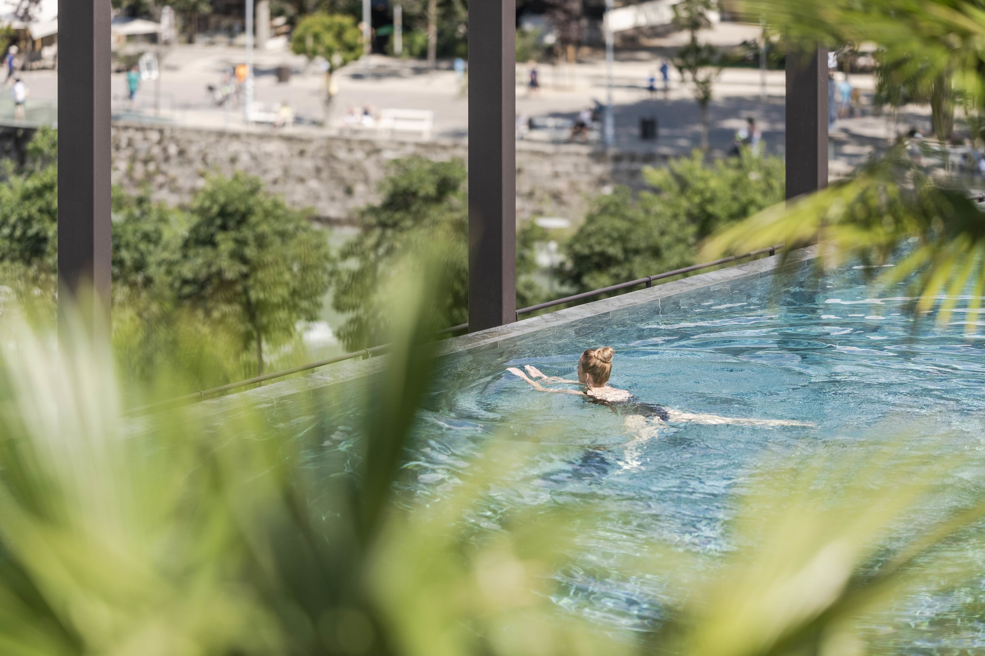 En person som simmar i en pool med utsikt över en strand och palmer i bakgrunden.