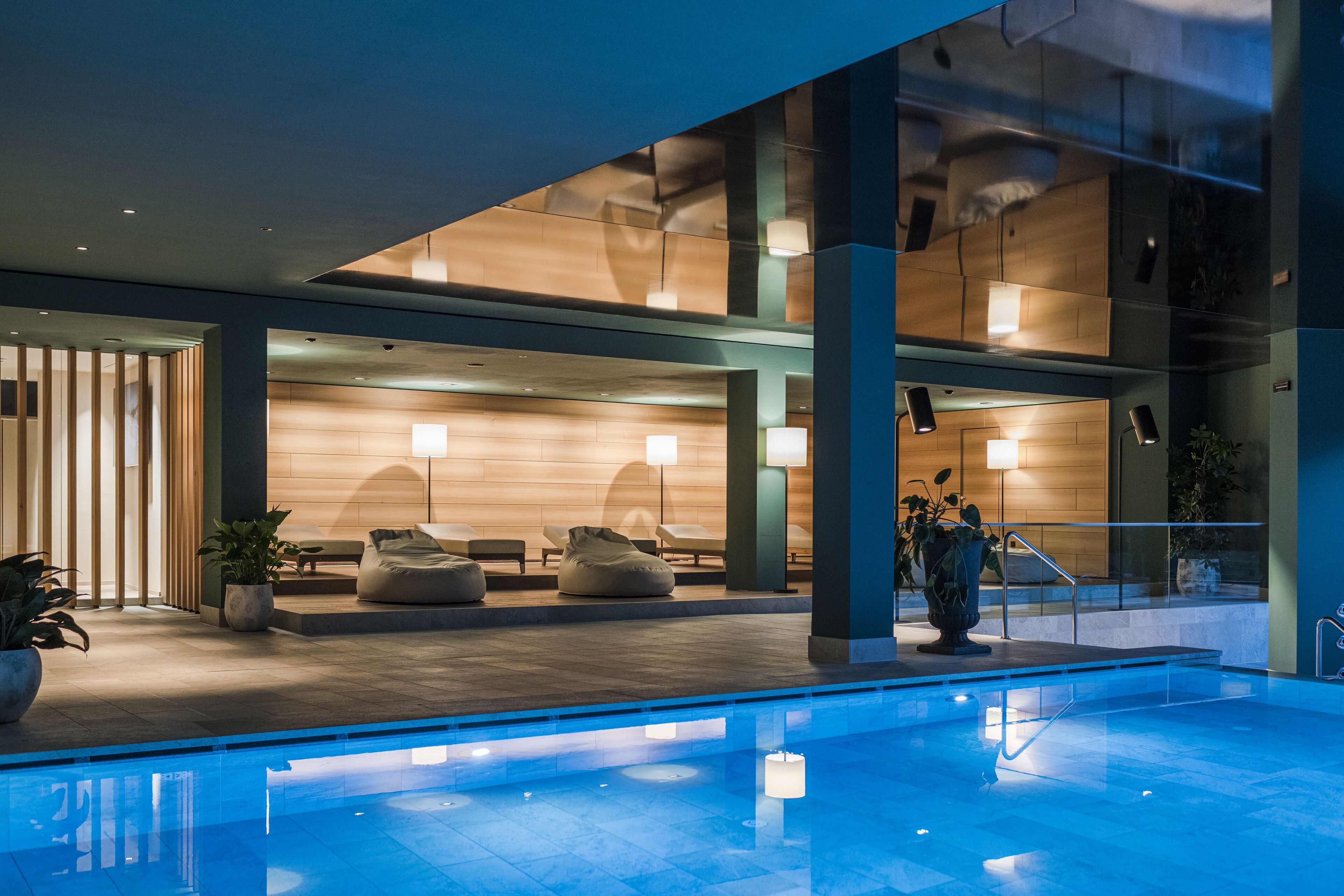 A modern indoor pool area with seating and a wooden reception desk.