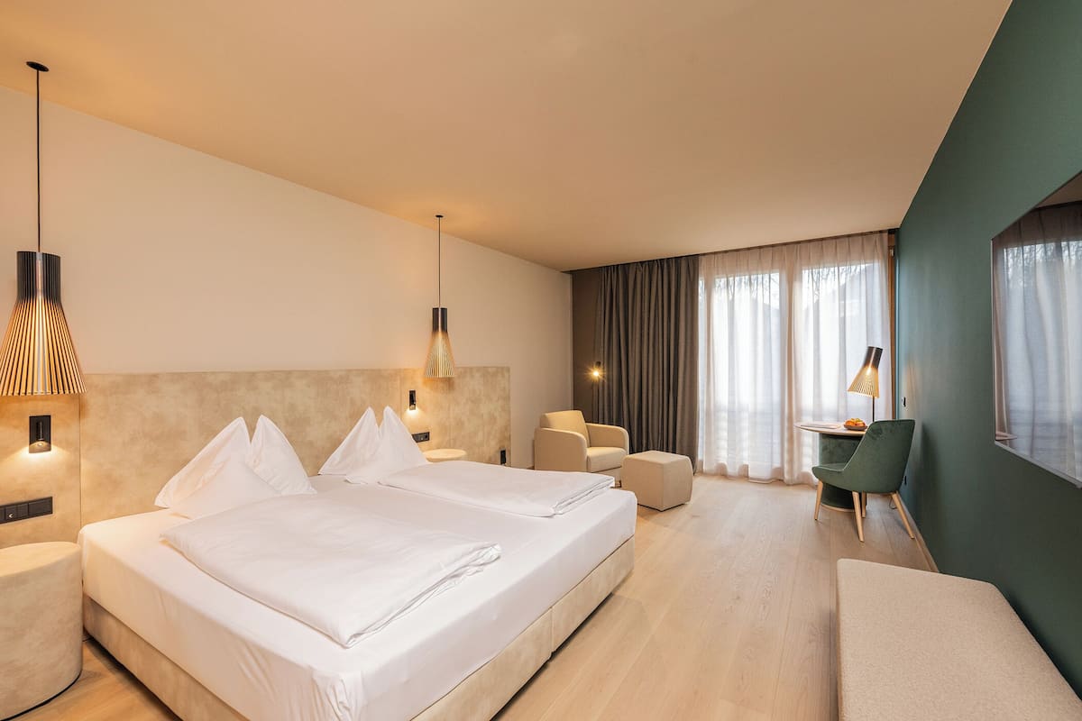 A hotel room with two beds, a desk, a chair, and a lamp.