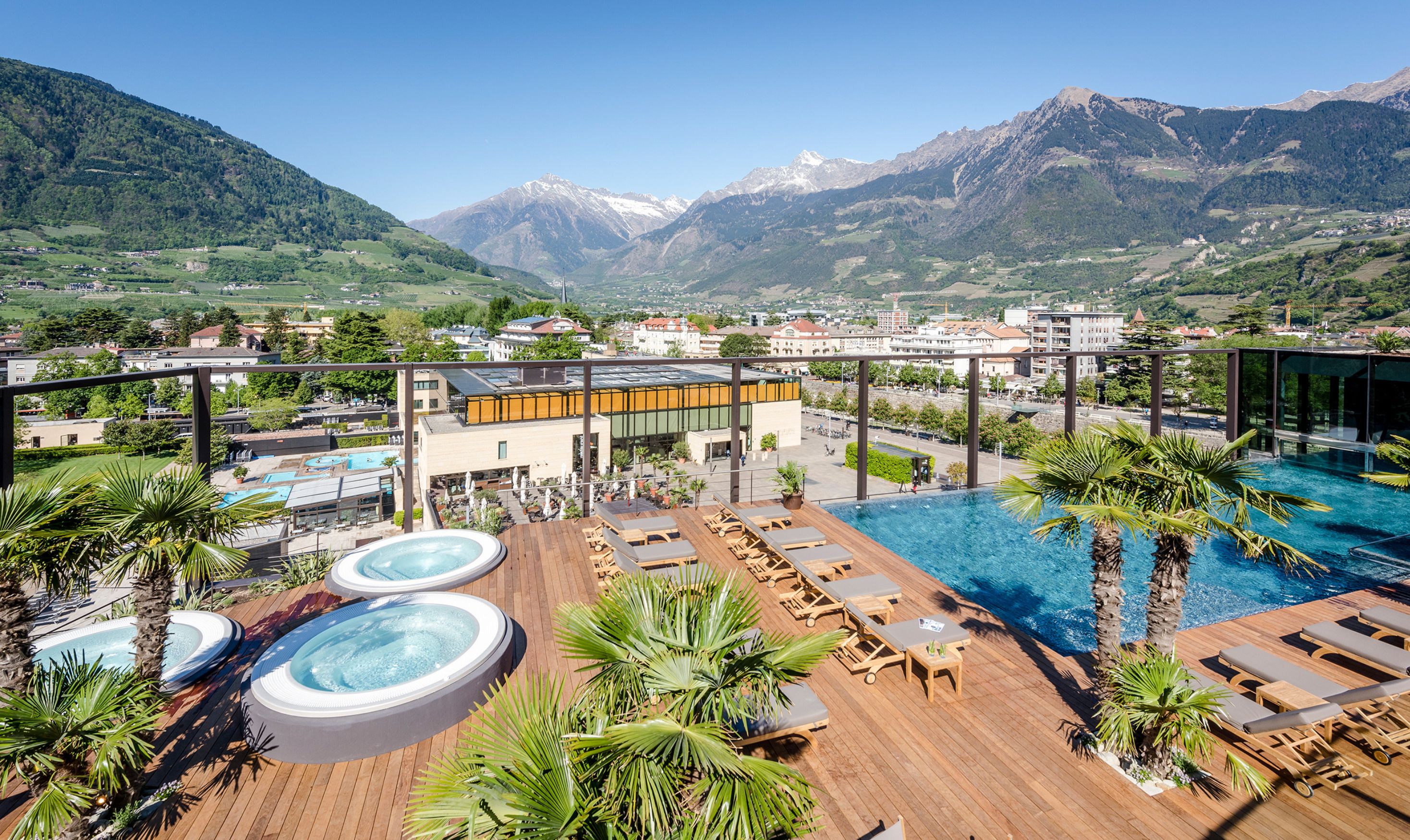 Área de piscina en la azotea con jacuzzis, sillas de descanso y vistas a las montañas.