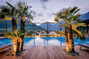 Piscina infinita con terraza de madera, palmeras y vista a la montaña.