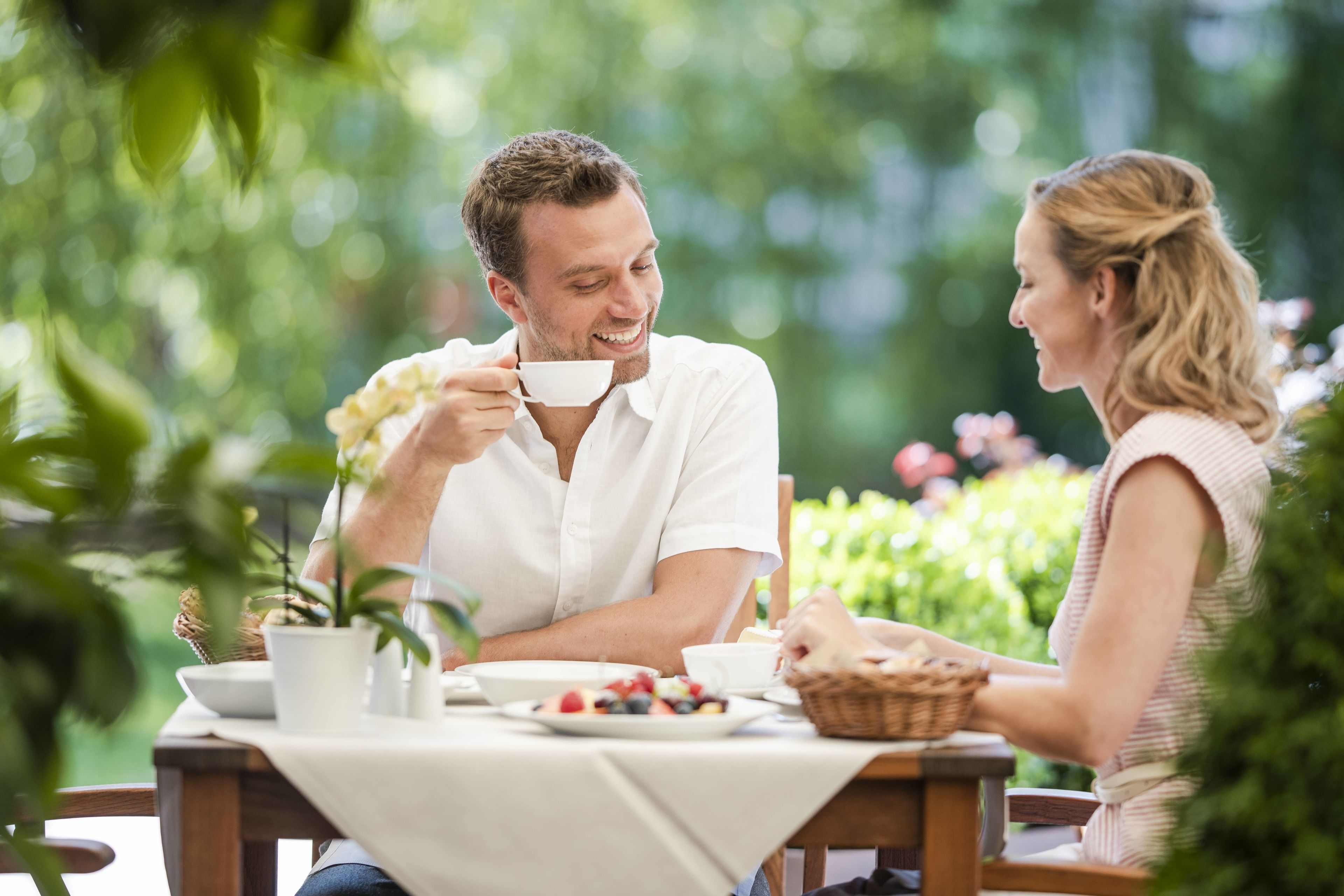 Una pareja cenando en una mesa al aire libre con mantel blanco, rodeada de follaje.