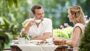 Una pareja cenando en una mesa al aire libre con mantel blanco, rodeada de follaje.