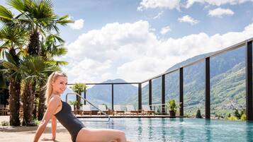 Mulher de biquíni perto de uma piscina, com vista para as montanhas.