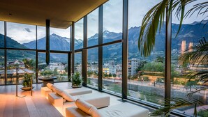 A modern interior with large windows, a wooden floor, and a seating area with cushions. - Hotel Therme Meran - Terme Merano (Merano)