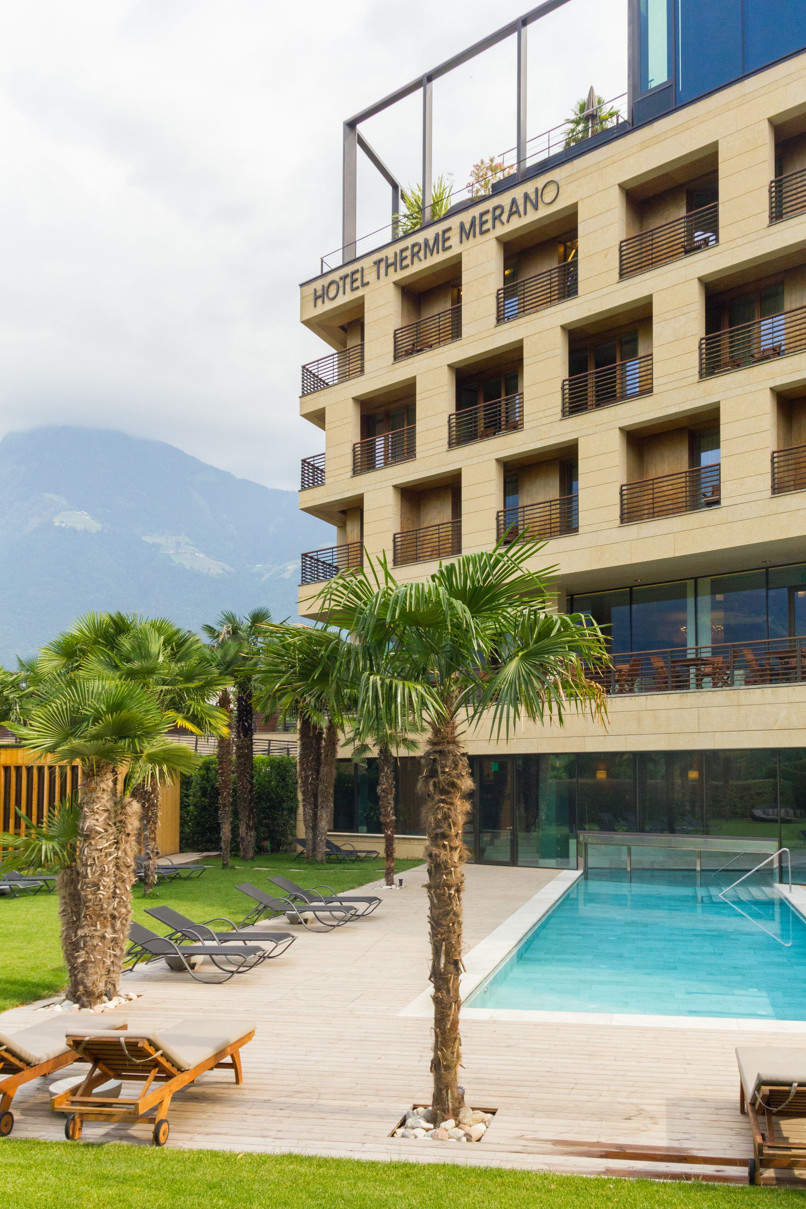 A hotel with a pool, palm trees, and a mountainous backdrop.