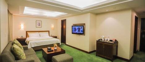 A hotel room with a bed, a sofa, a coffee table, a TV, and a small cabinet.