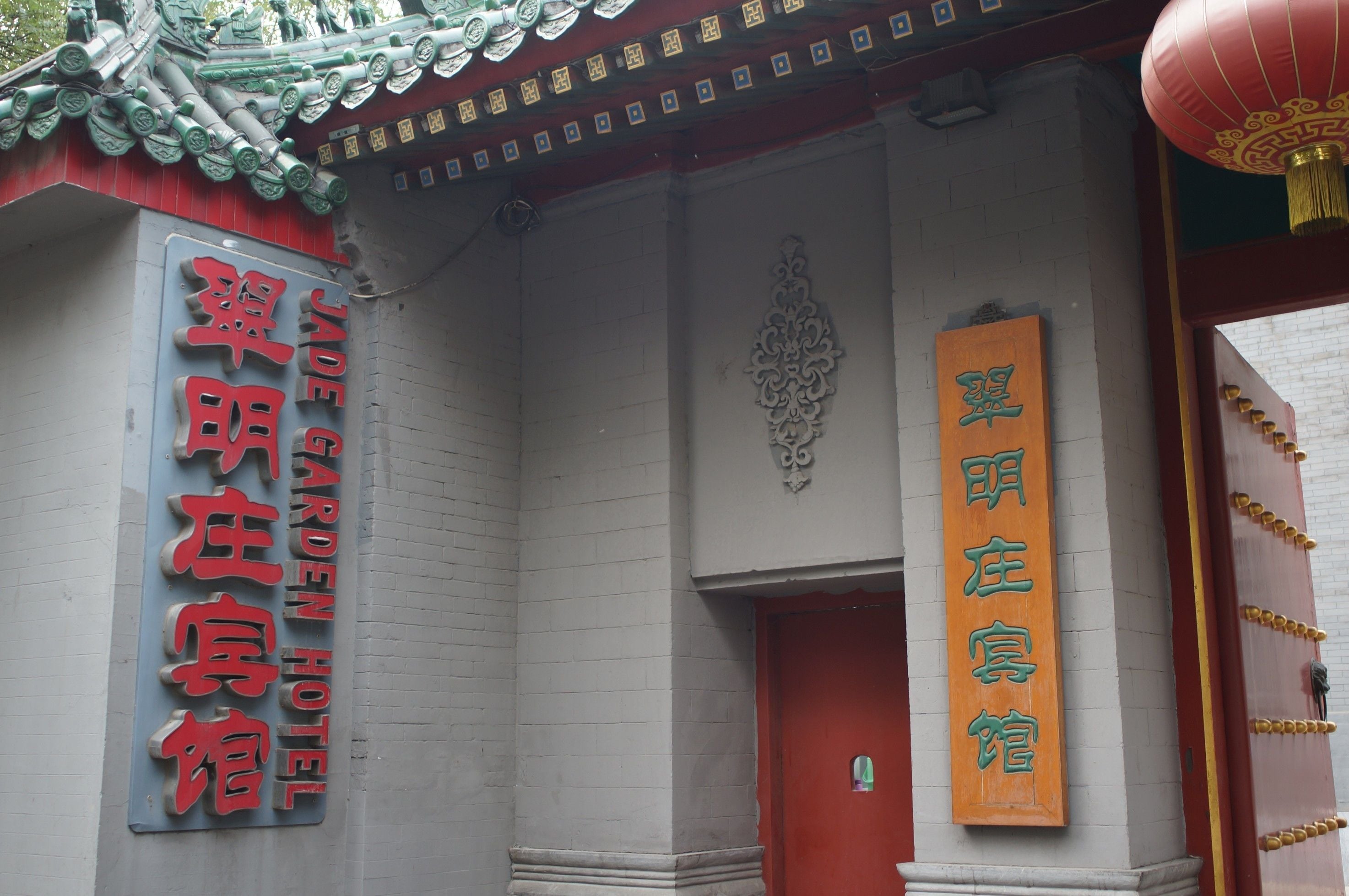 Entrada de hotel de estilo arquitectónico tradicional, con una puerta roja y un letrero con caracteres chinos.