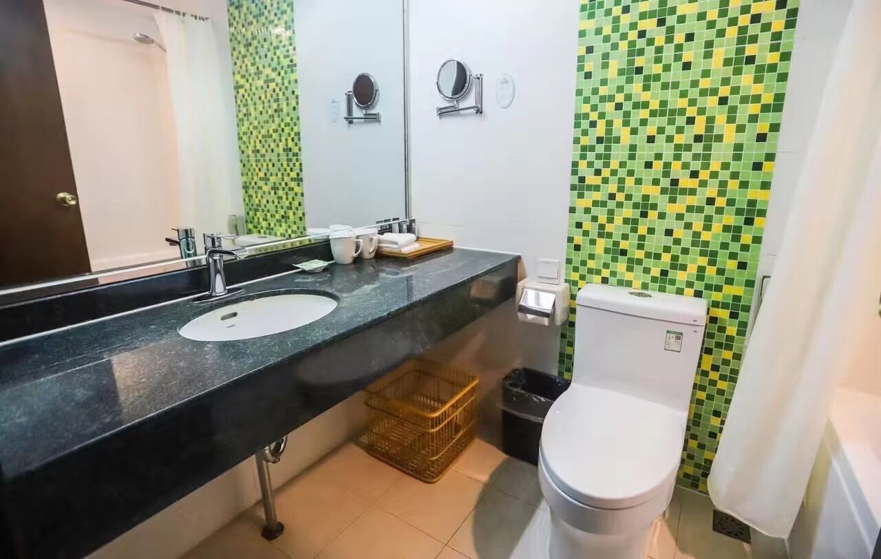 Casa de banho com bancada preta, duas pias, sanita e espelho.