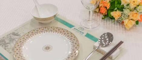 Une table dressée avec une assiette blanche, un bol, un verre, une cuillère et des baguettes, accompagnée d’un bouquet de fleurs.